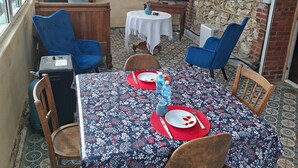A dining area with a table set for two, a television, and a stone wall. - 1 studio apartment for rent in Villa Amenaide: 1 bedroom, plus kitchen, dining room, and living room (Roisel)
