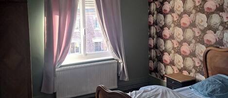 Un dormitorio con una cama de madera, un radiador, una ventana con cortinas y un papel tapiz floral.