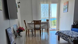 Ein Wohnzimmer mit Essbereich, einem Wandfernseher, einer Couch und einem Tisch mit Stühlen.