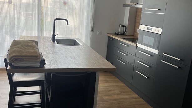 A modern kitchen with a central island, dark cabinetry, and a window with sheer curtains.