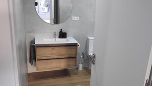 A bathroom with a wooden vanity, a round mirror, a white sink, and a toilet.