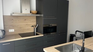A modern kitchen with dark cabinetry, a wooden backsplash, a stainless steel sink, and a built-in oven.