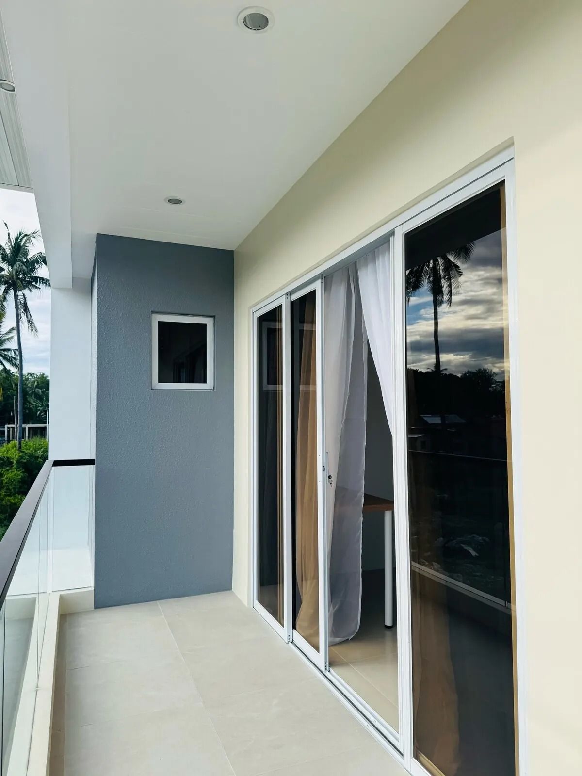 A balcony with a sliding glass door, a small window, and a view of palm trees.
