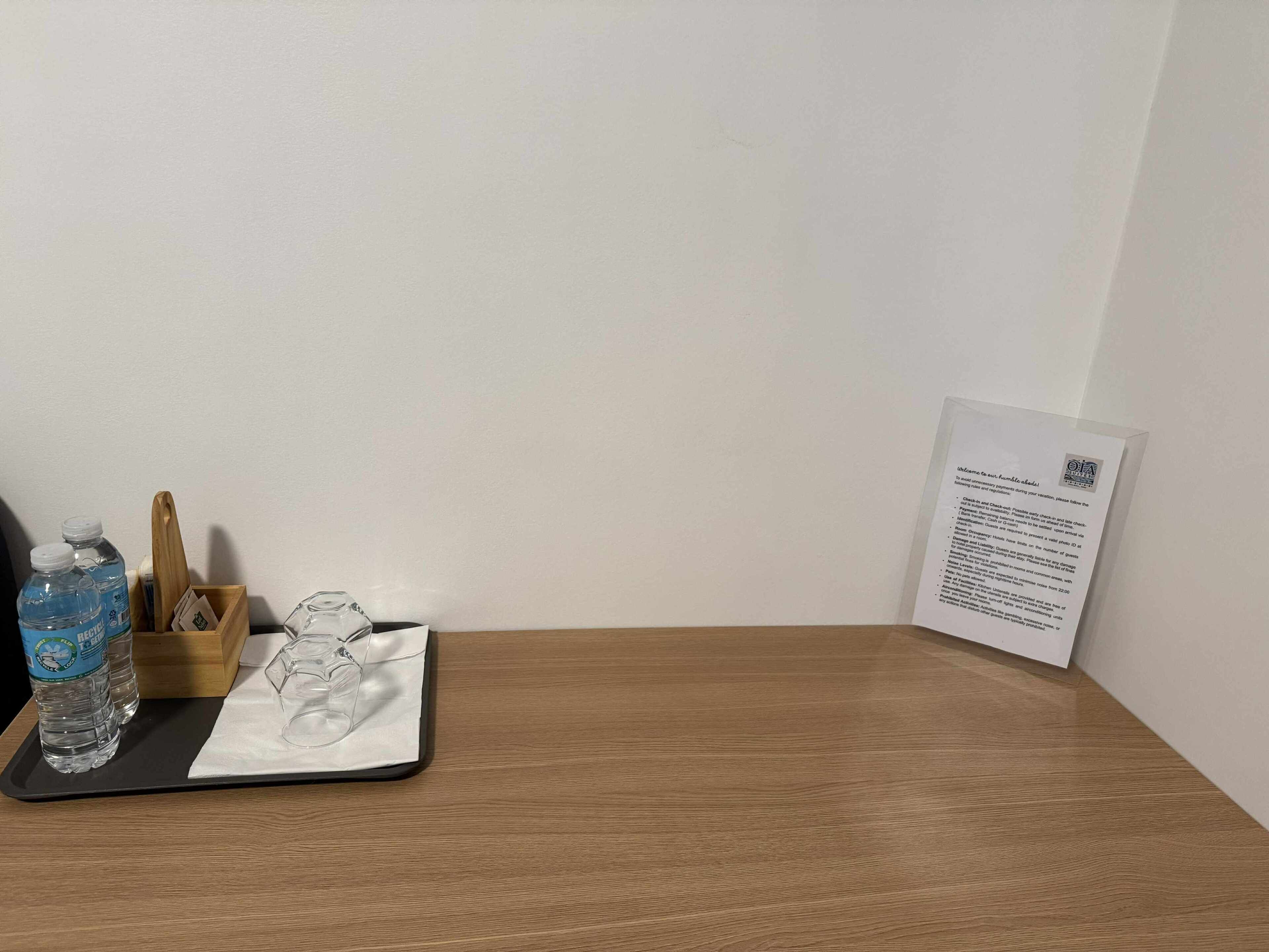 Ett träbord med ett bricka som innehåller vattenflaskor, ett glas och ett kort. En välkomstskylt syns på väggen.