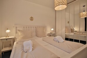 Ein Hotelzimmer mit einem großen Bett, zwei Nachttischen mit Lampen, einem Spiegel und einer Wanduhr.
