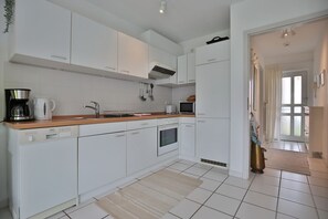 A modern kitchen with white cabinets, a wooden countertop, a Bosch dishwasher, a stove, and a microwave.