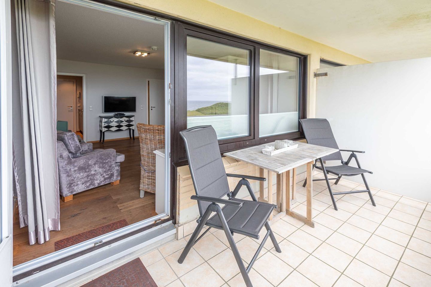 A balcony with a table and chairs, a sofa, and a TV in the background.