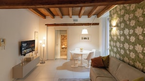 Una sala de estar acogedora con un sofá, una mesa de comedor con sillas y un televisor instalado en la pared.