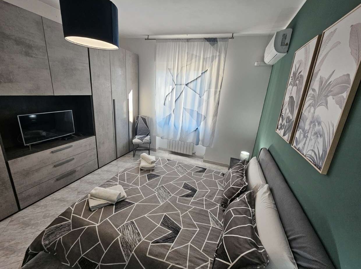 Ein modernes Schlafzimmer mit einem Bett mit geometrischem Muster, einem Flachbildfernseher, einem Sessel und Kunstwerken an den Wänden.