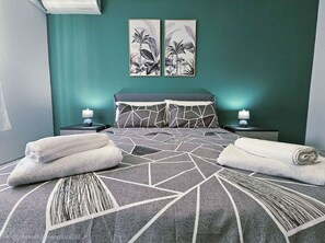 Habitación de hotel con una cama, dos mesitas de noche, una lámpara y dos cuadros colgados en la pared.