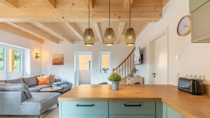 A modern kitchen with a wooden countertop, a built-in stove, and a sink. There is a dining area with a gray sofa and a small table.