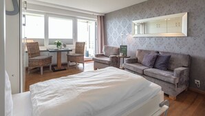 A hotel room with a bed, a sofa, a dining table with chairs, and a large mirror. - 1-room apartment with sea view and approx. 34 m² living space, for up to 2 people (Wenningstedt-Braderup (Sylt))