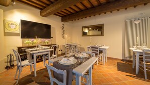 A dining area with wooden tables and chairs, a television mounted on the wall, and a tiled floor. - Apartment with hot tub, A/C, WIFI, sauna, private pool, TV, patio, panoramic view, close to Siena (Monteriggioni)