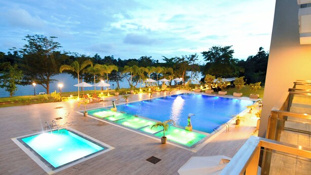 Ein Poolbereich mit zwei separaten Pools, umgeben von Kübelpflanzen und Sonnenschirmen, mit Blick auf ein Gewässer und Bäume im Hintergrund.