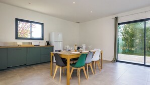 Een moderne keuken met een eethoek, met een groot raam, groene kastjes en een betegelde vloer.