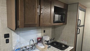 Cocina compacta con armarios de madera, microondas, refrigerador, pileta con grifo y cafetera.