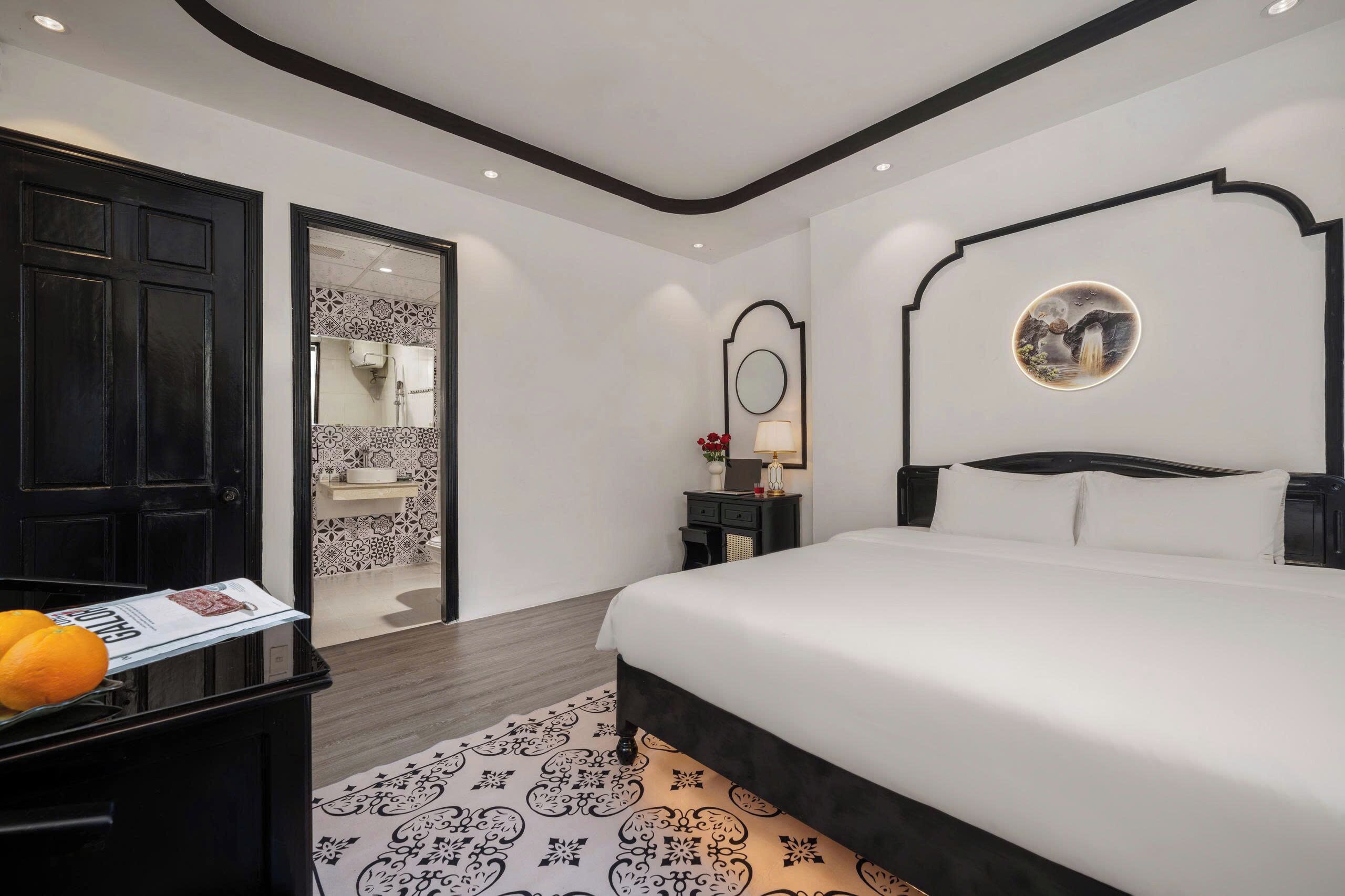 Una habitación de hotel moderna con una cama grande, una mesita de noche, un espejo y una puerta que da a un baño.