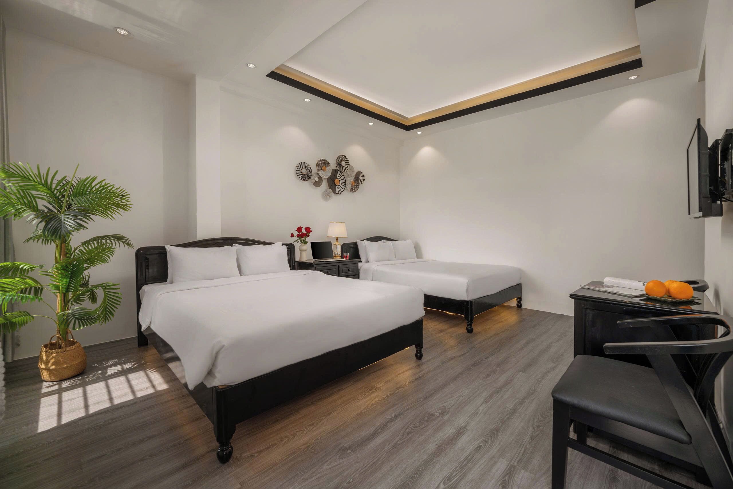 Une chambre d’hôtel moderne avec deux lits, un bureau, une chaise, une plante en pot et des œuvres d’art décoratives au mur.