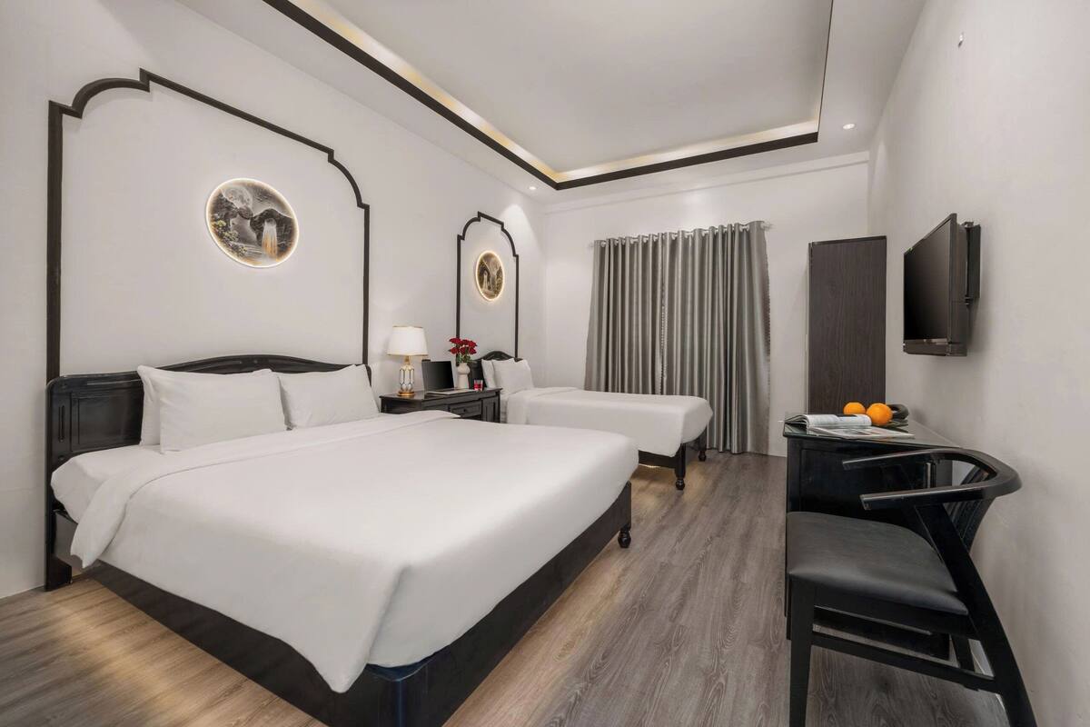 Une chambre d’hôtel avec un grand lit, deux tables de chevet, un bureau avec une chaise, une télévision et une fenêtre avec des rideaux.