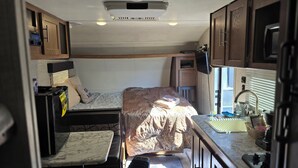 A compact RV interior with a bed, kitchenette, and a small seating area. - Adventurer, RV in delightful Atlanta with AC (Atlanta)
