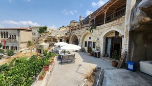 A courtyard with outdoor seating, stone buildings, and a view of the surrounding landscape. - Deep Cave House  (Urgup)