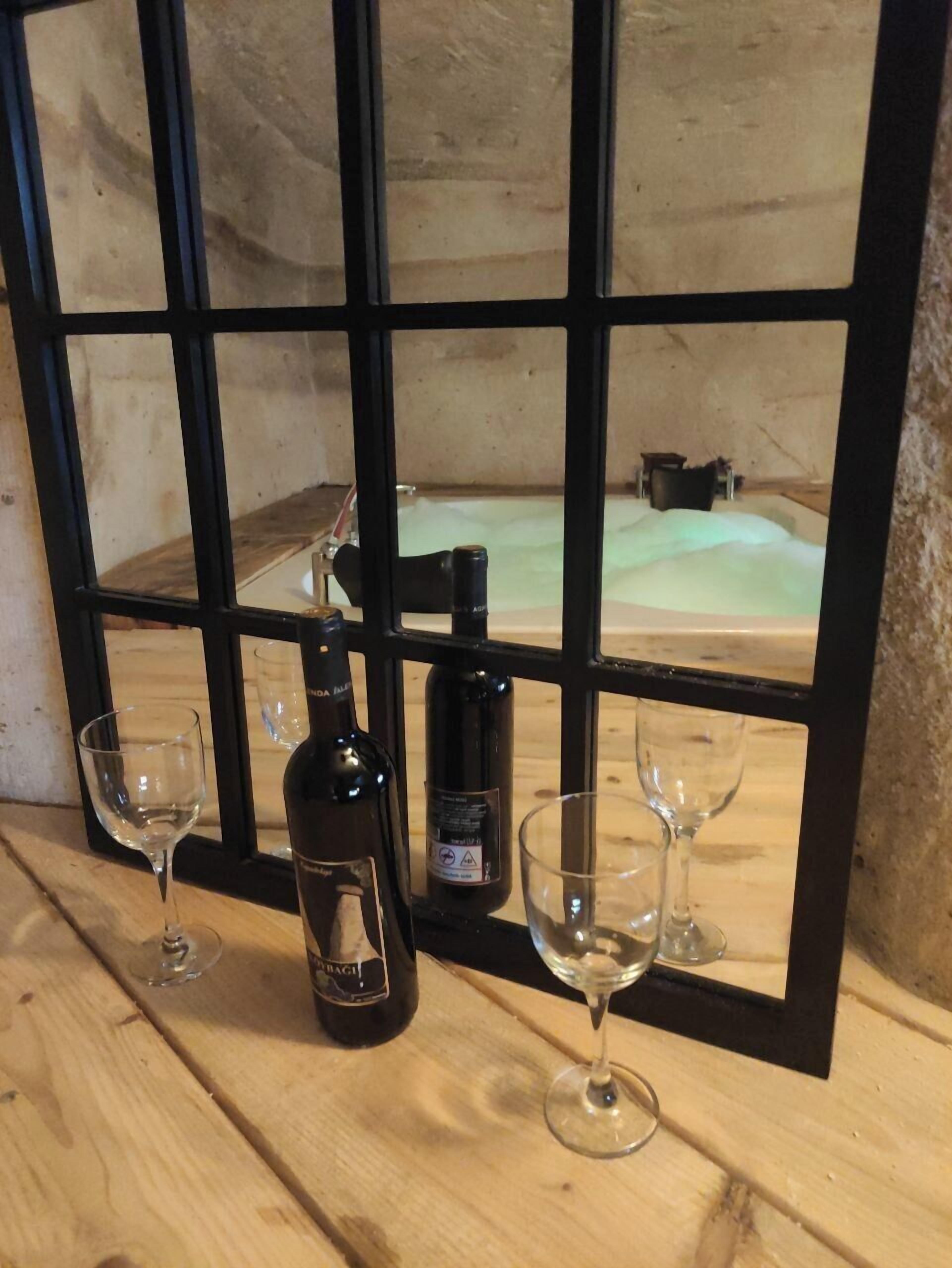 Una mesa de madera con una botella de vino y dos copas, ubicada frente a una ventana que da a un área de spa.
