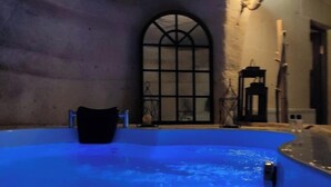 A dimly lit indoor swimming pool with a blue hue, a large arched window, and a stone wall. - Deep Cave House  (Urgup)