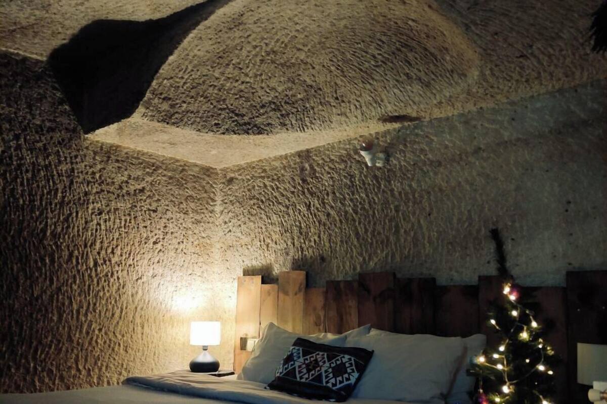 Ein gemütliches Zimmer mit Bett, Holz-Kopfteil, Nachttisch, Lampe und einem Weihnachtsbaum.