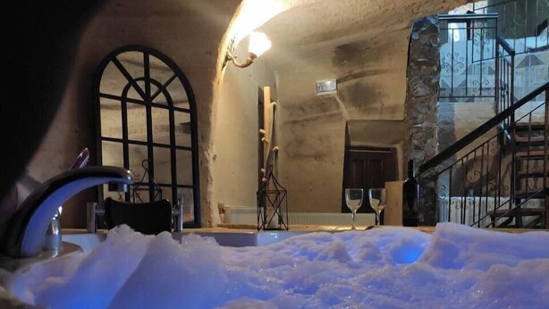 A rustic interior with a stone wall, a wooden bench, a small table with a wine glass, and a staircase leading to an upper level. - Deep Cave House  (Urgup)