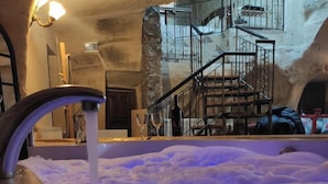 A hot tub with a flowing water faucet, a staircase with a metal railing, and a stone wall in the background. - Deep Cave House  (Urgup)