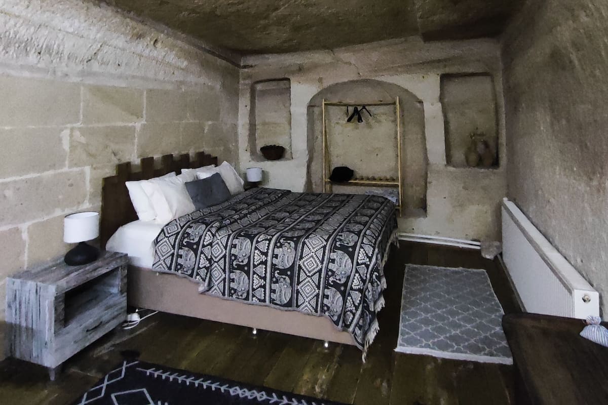 Ein rustikales Schlafzimmer mit Steinwand, einem hölzernen Bett, einer kleinen Ablage und einer Bank.