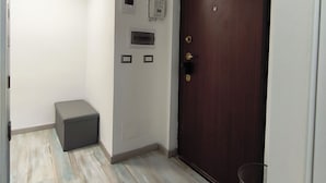 A hallway with a wooden door, a small bench, and a trash bin.