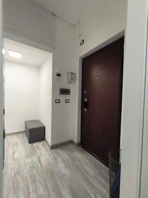 Un couloir avec une porte en bois, un petit banc et une poubelle.