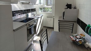 A modern kitchen with a built-in oven, a dining table with chairs, and a window with blinds.