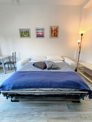 A bed with a blue cover, white pillows, and two framed pictures on the wall.