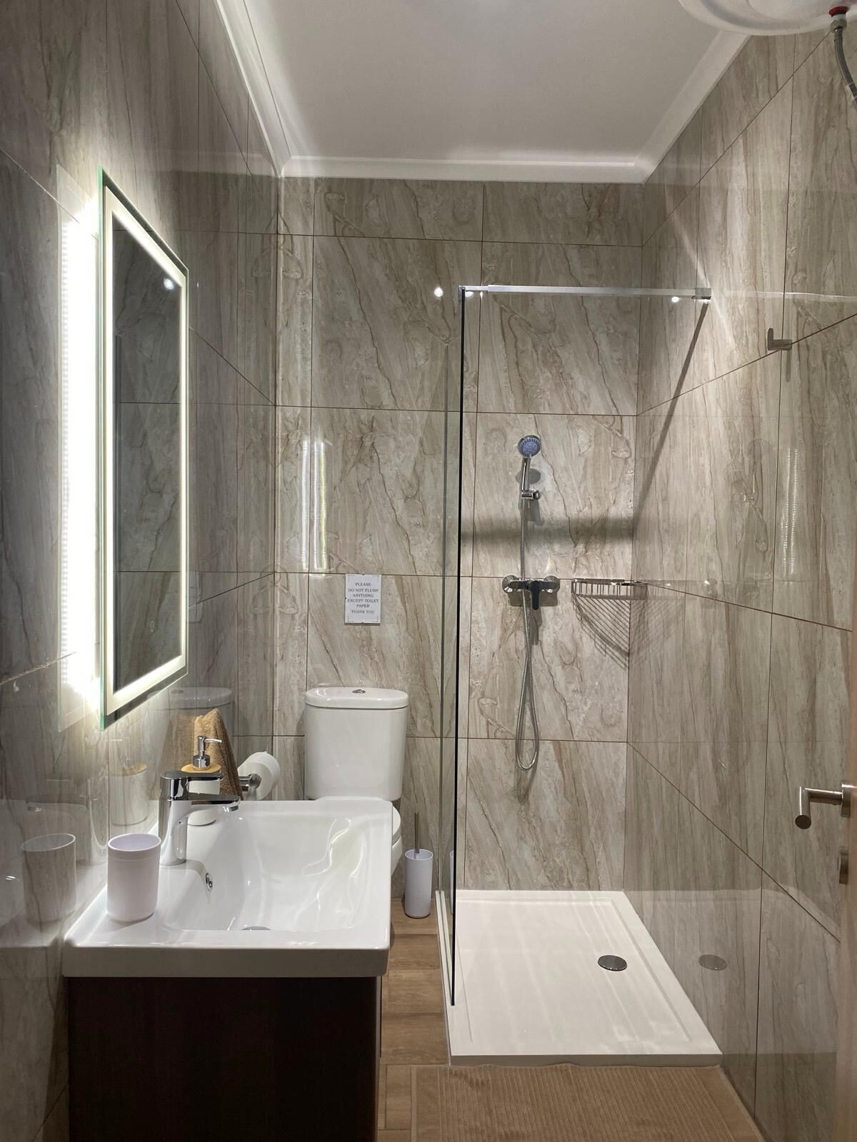 Une salle de bain moderne avec une douche à parois de verre, un grand miroir, un lavabo blanc et des toilettes.
