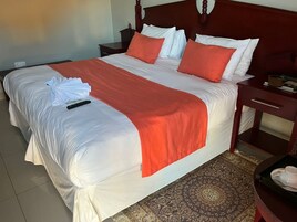 Una cama bien hecha con ropa de cama blanca y naranja, un control remoto y una toalla doblada sobre la cama.