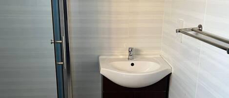 A bathroom with a glass shower enclosure, a white sink, dark cabinets, and a patterned floor.
