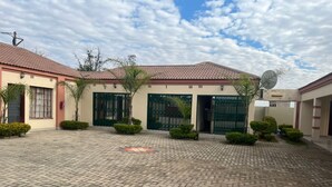 A courtyard with a paved walkway, a building with a tiled roof, and a satellite dish. - Kalimba Guesthouse (Gaborone)