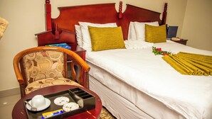 A hotel room with a large bed, wooden headboard, and a small table with a tray of breakfast items. - Kalimba Guesthouse (Gaborone)