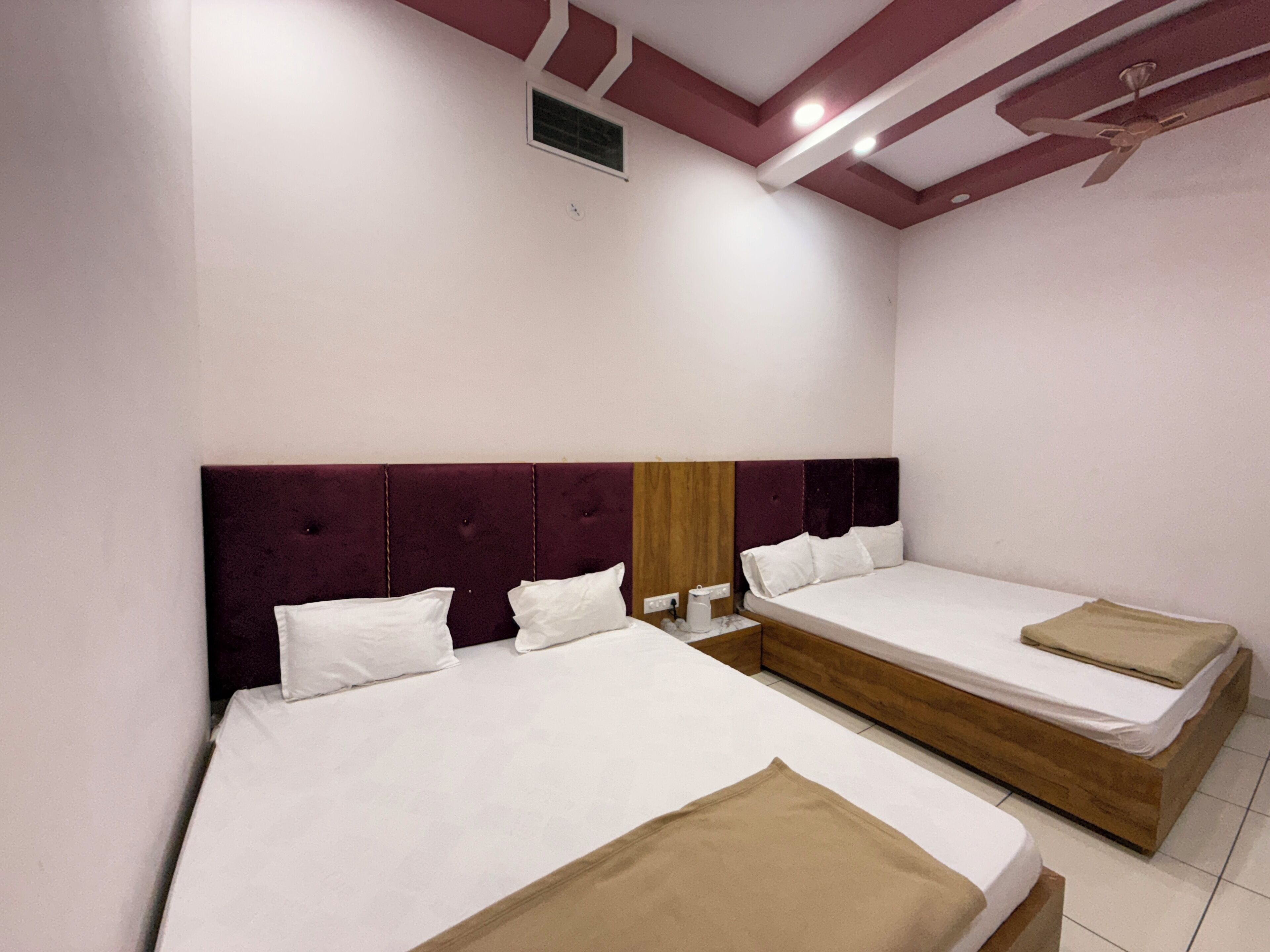 Habitación de hotel con dos camas individuales, cabecera de madera, mesita de noche pequeña con lámpara y ventilador de techo.