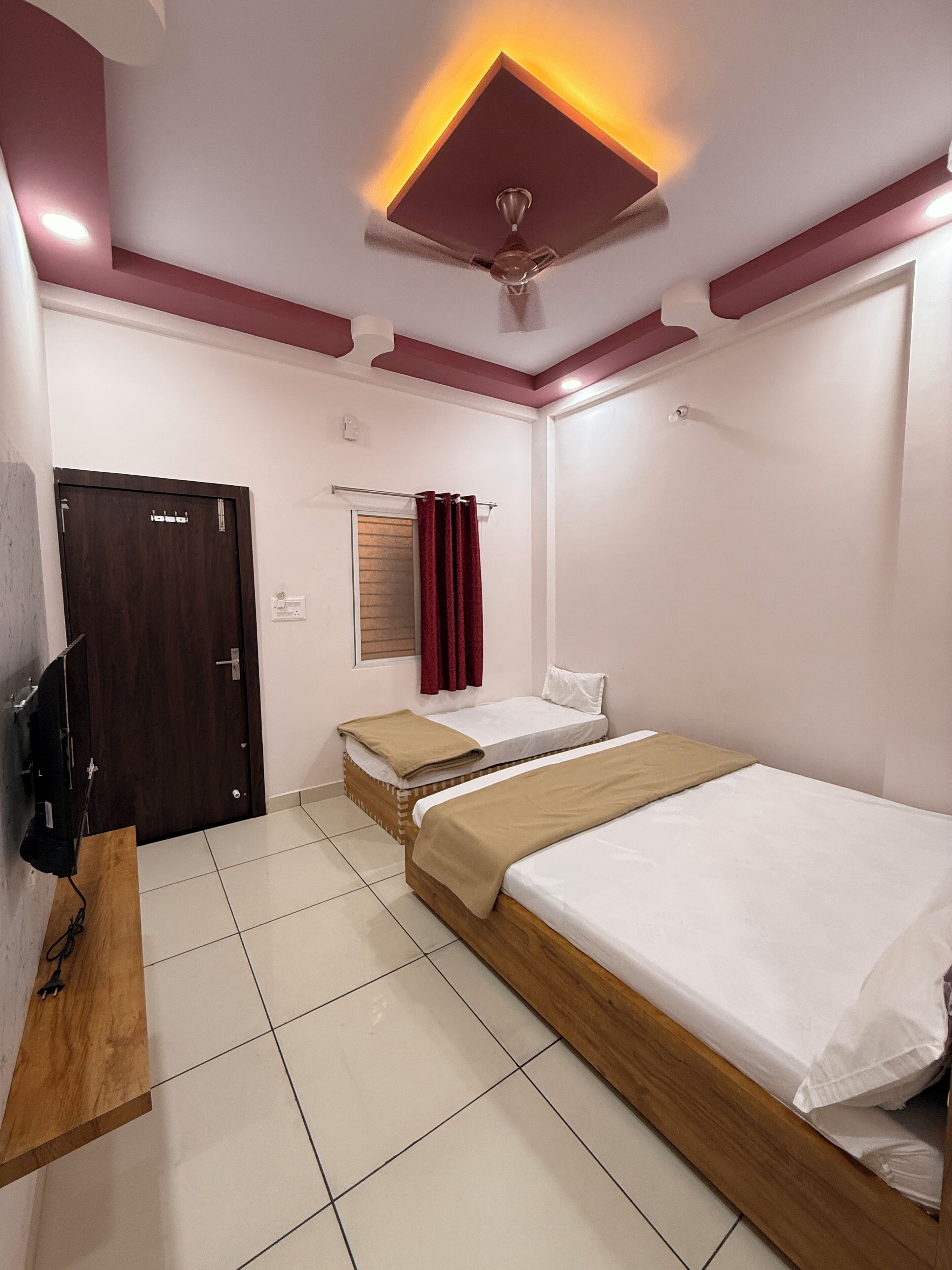 A hotel room with two beds, a wooden desk, a TV, a ceiling fan, and a door.