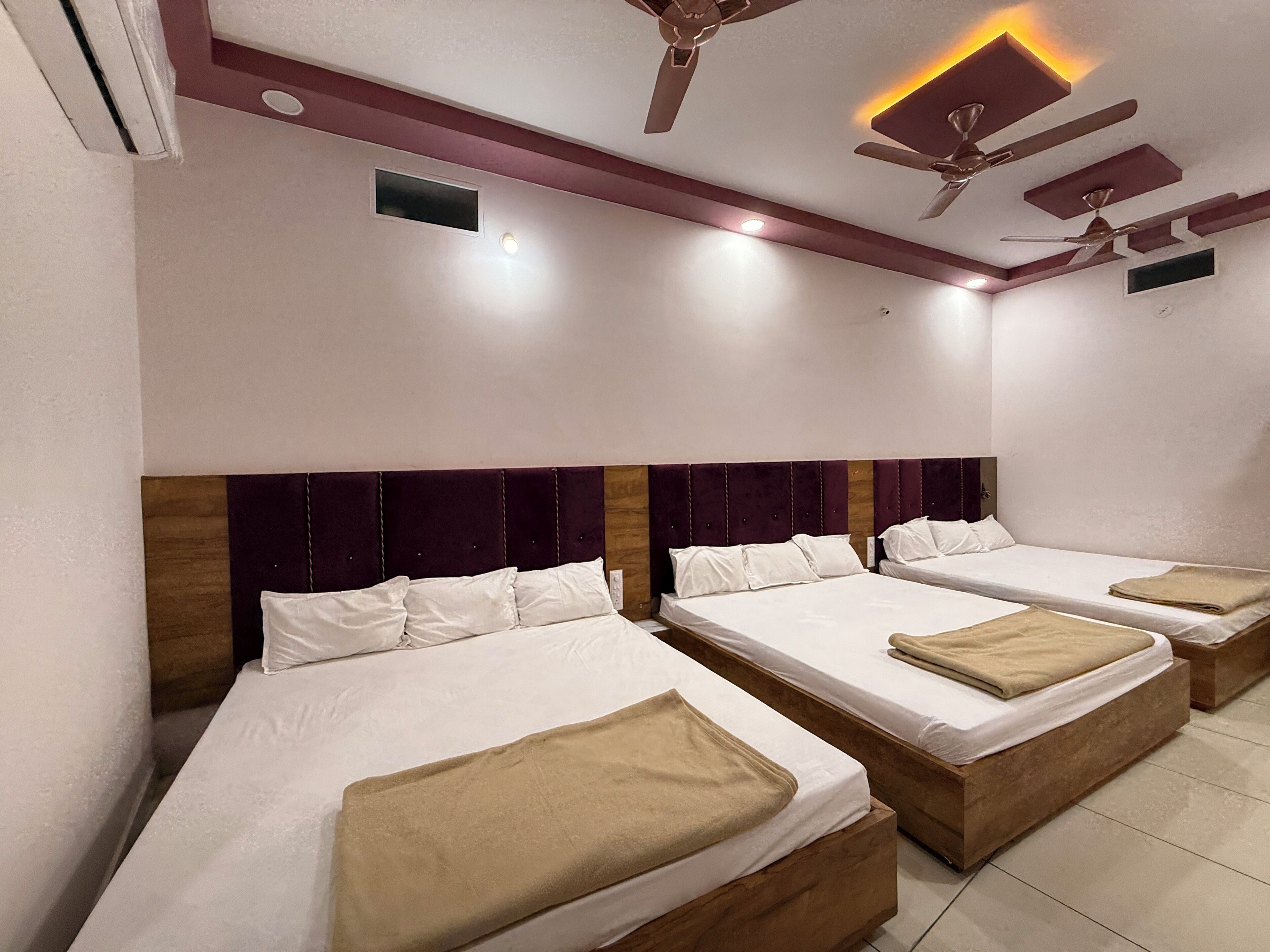 Habitación de hotel con tres camas, cada una con cabecero de madera y ropa de cama blanca. Cuenta con ventiladores de techo e iluminación empotrada.