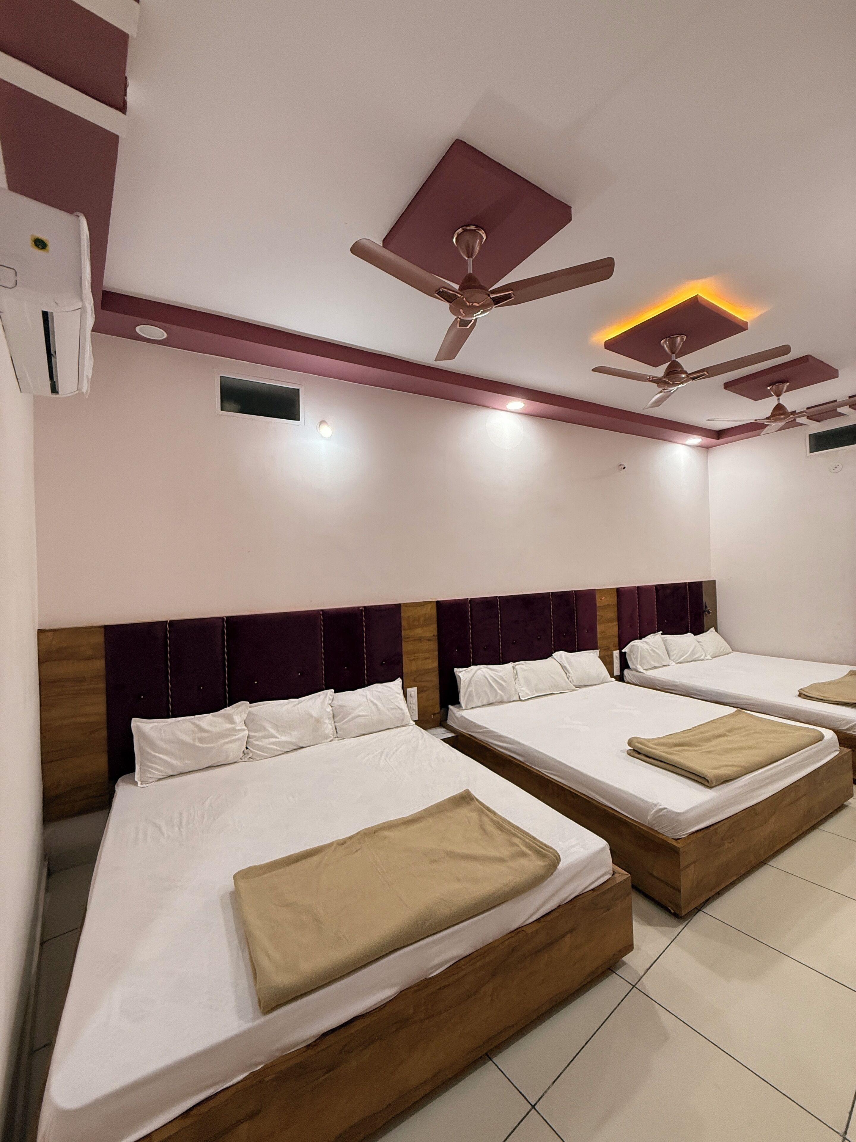 Habitación de hotel con tres camas, cada una con cabecero de madera y ropa de cama blanca. Incluye ventiladores de techo e iluminación empotrada.