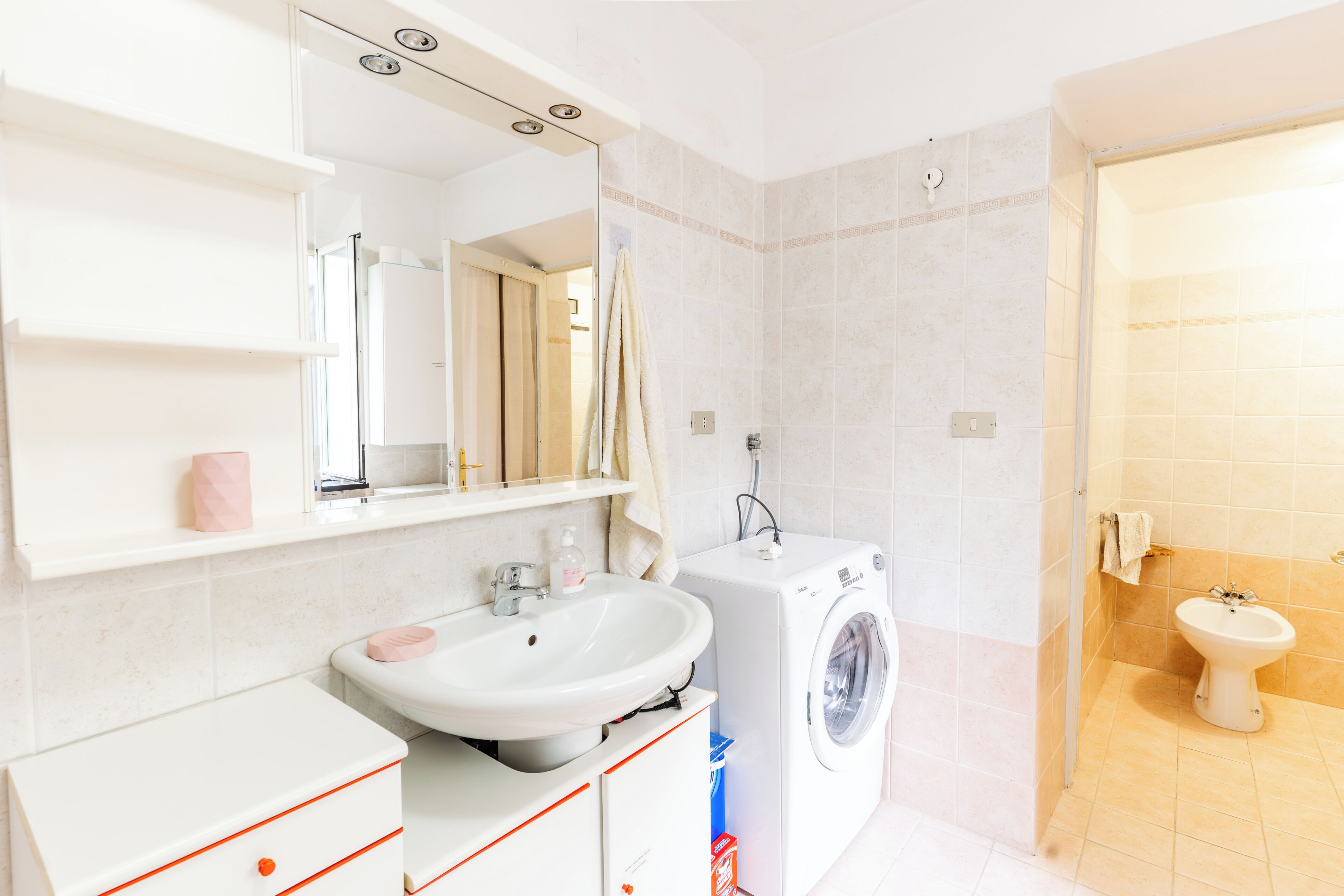 Une salle de bain moderne équipée d’un lavabo, d’un miroir, d’un lave-linge et de toilettes.