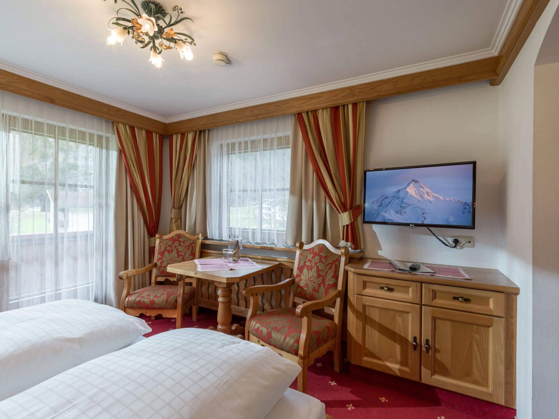 A hotel room with two beds, a wooden desk with a television, and a window with curtains.