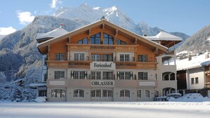 A multi-story hotel with a wooden facade and balconies, named "Ferienhof" and "OBLASSER," set against a snowy mountain backdrop. - Ferienhof Oblasser (Mayrhofen)