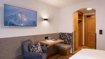 A cozy room with a bed, a seating area with a table, a wall-mounted TV, and a wooden wardrobe.