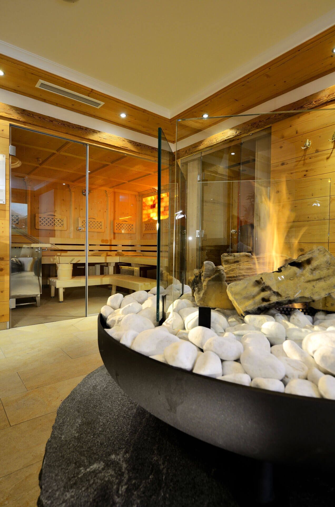 A modern interior with a stone fireplace surrounded by white pebbles, wooden beams on the ceiling, and a glass partition.