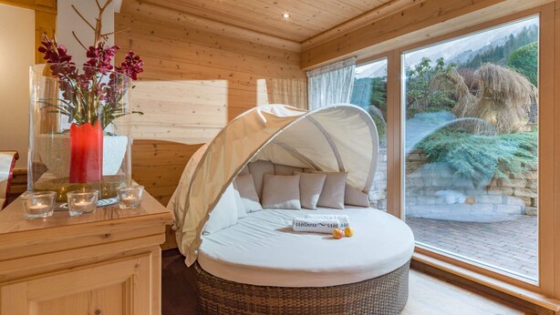 A cozy bedroom with a round bed, a canopy, a vase with flowers, and a view of the outdoors. - Ferienhof Oblasser (Mayrhofen)